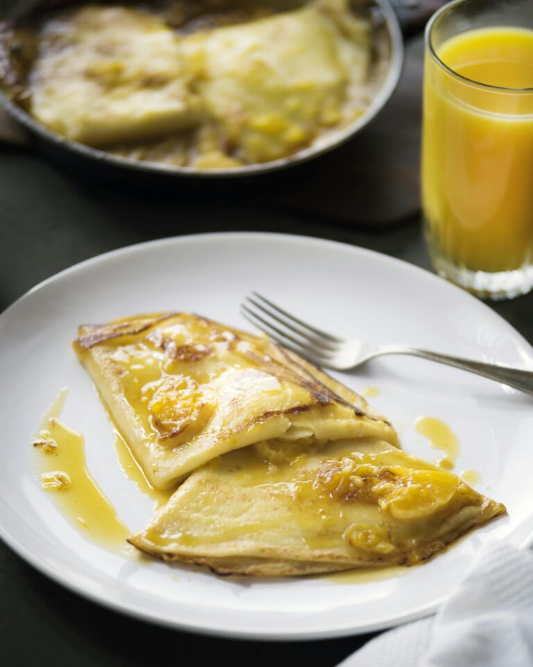 Appetizing crepes topped with jam served with fresh orange juice, creating a bright breakfast setup.