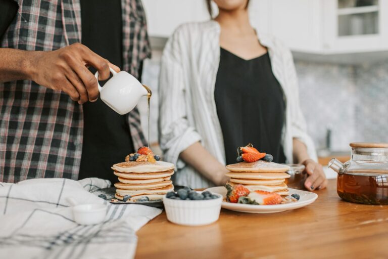 Close-up of pancakes topped with fresh berries and syrup pouring on them.