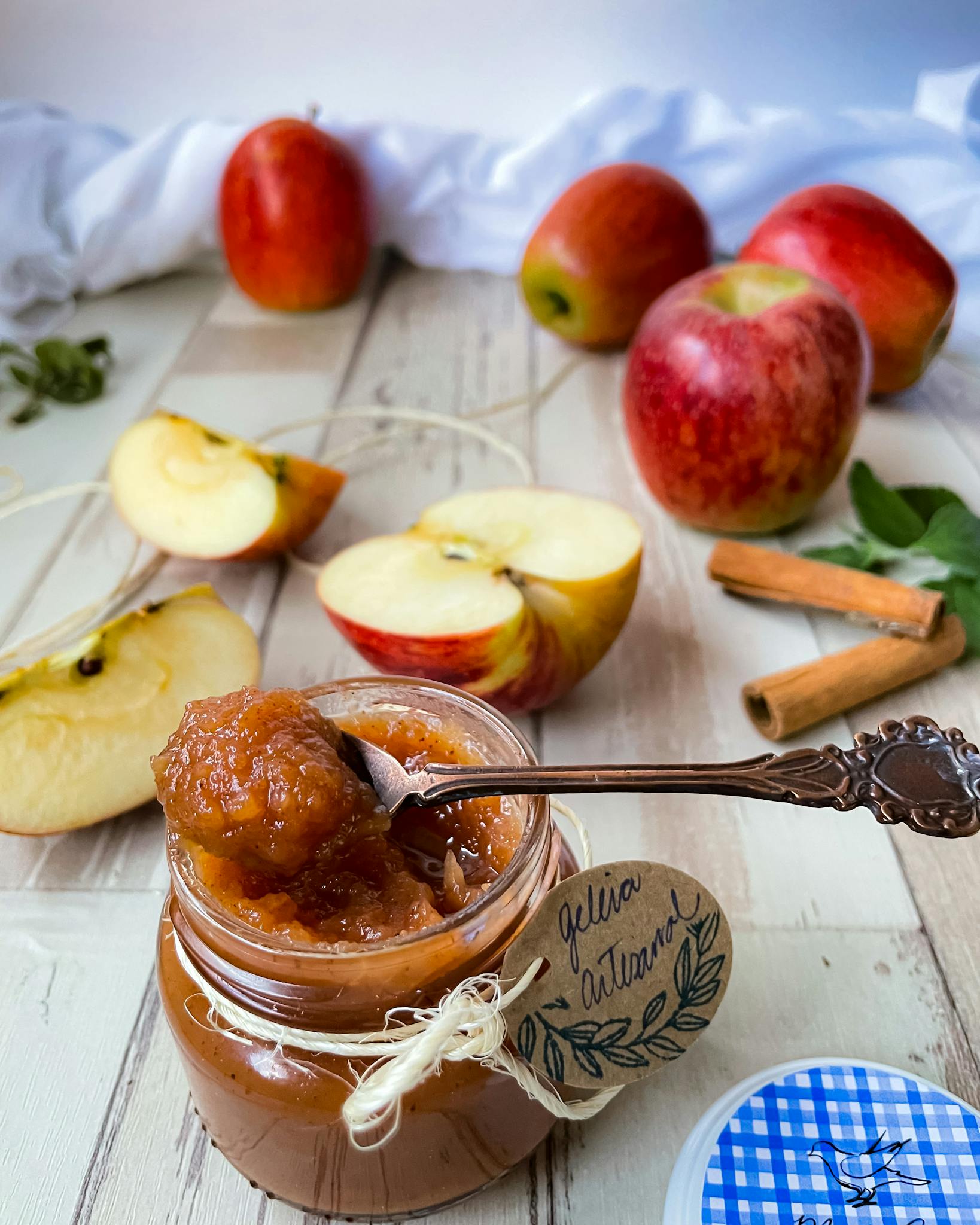 Delicious homemade apple jam in a jar with fresh apples and cinnamon sticks.