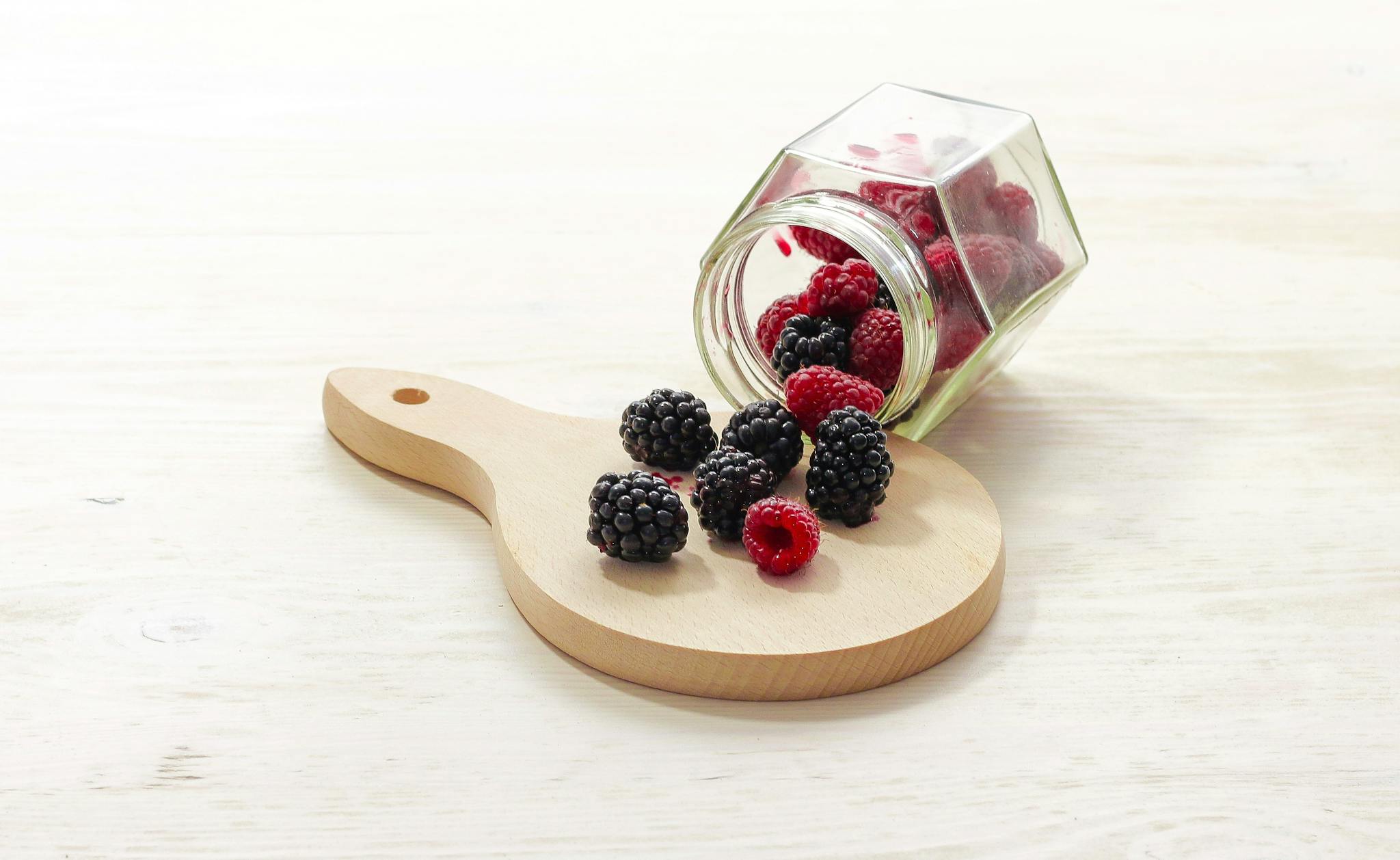Tasty mix of fresh blackberries and raspberries spilling from a jar onto a wooden board, perfect for healthy eating.